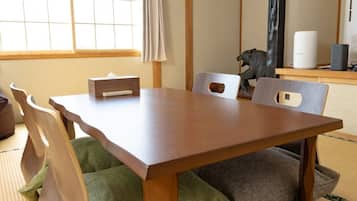 A traditional Japanese-style dining room with tatami mat flooring, a low wooden table, and simple wooden chairs.