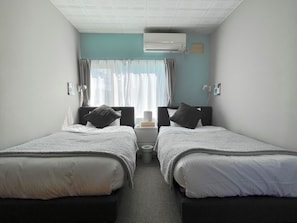 A hotel room with two single beds, a small bedside table, an air conditioning unit, and a window with curtains. - FURANO RETREAT (Furano)