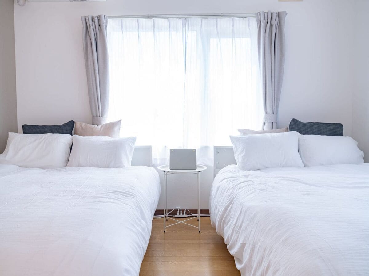 A hotel room with two beds, a small table, and a window with curtains.