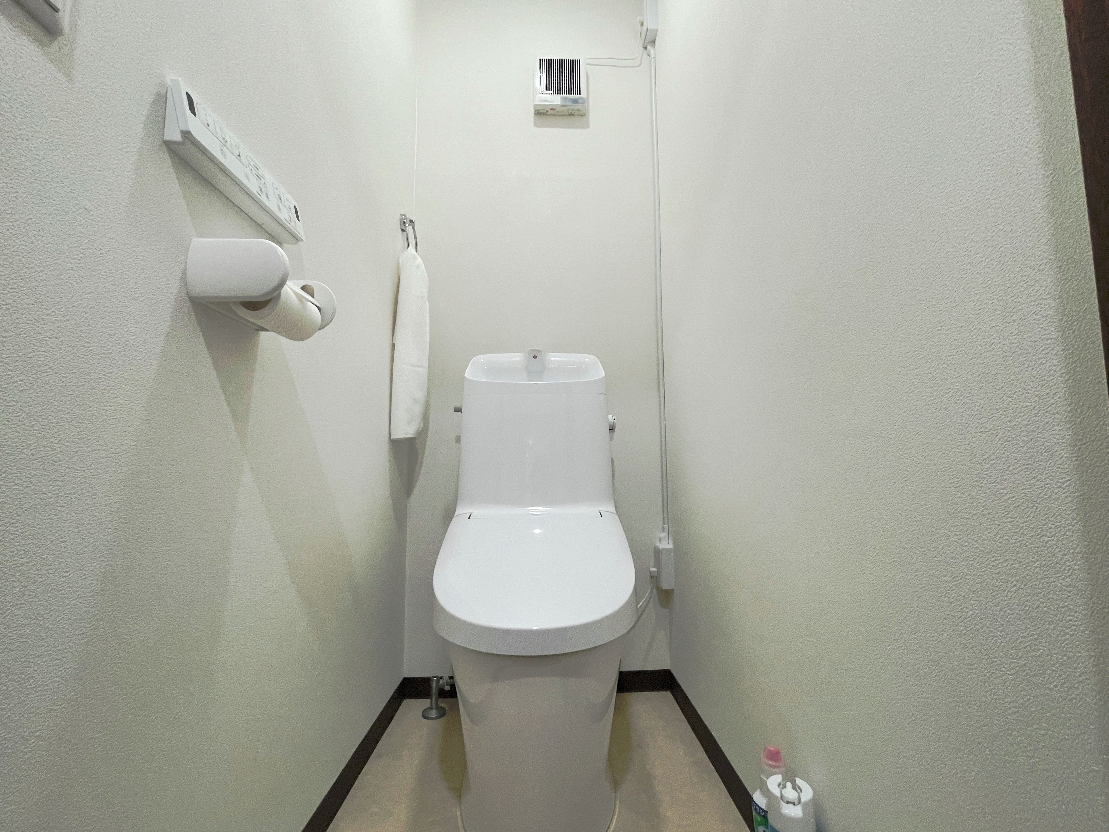 A small, white bathroom with a toilet, a hand dryer, and a towel hanging on a hook.