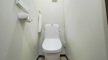 A small, white bathroom with a toilet, a hand dryer, and a towel hanging on a hook.
