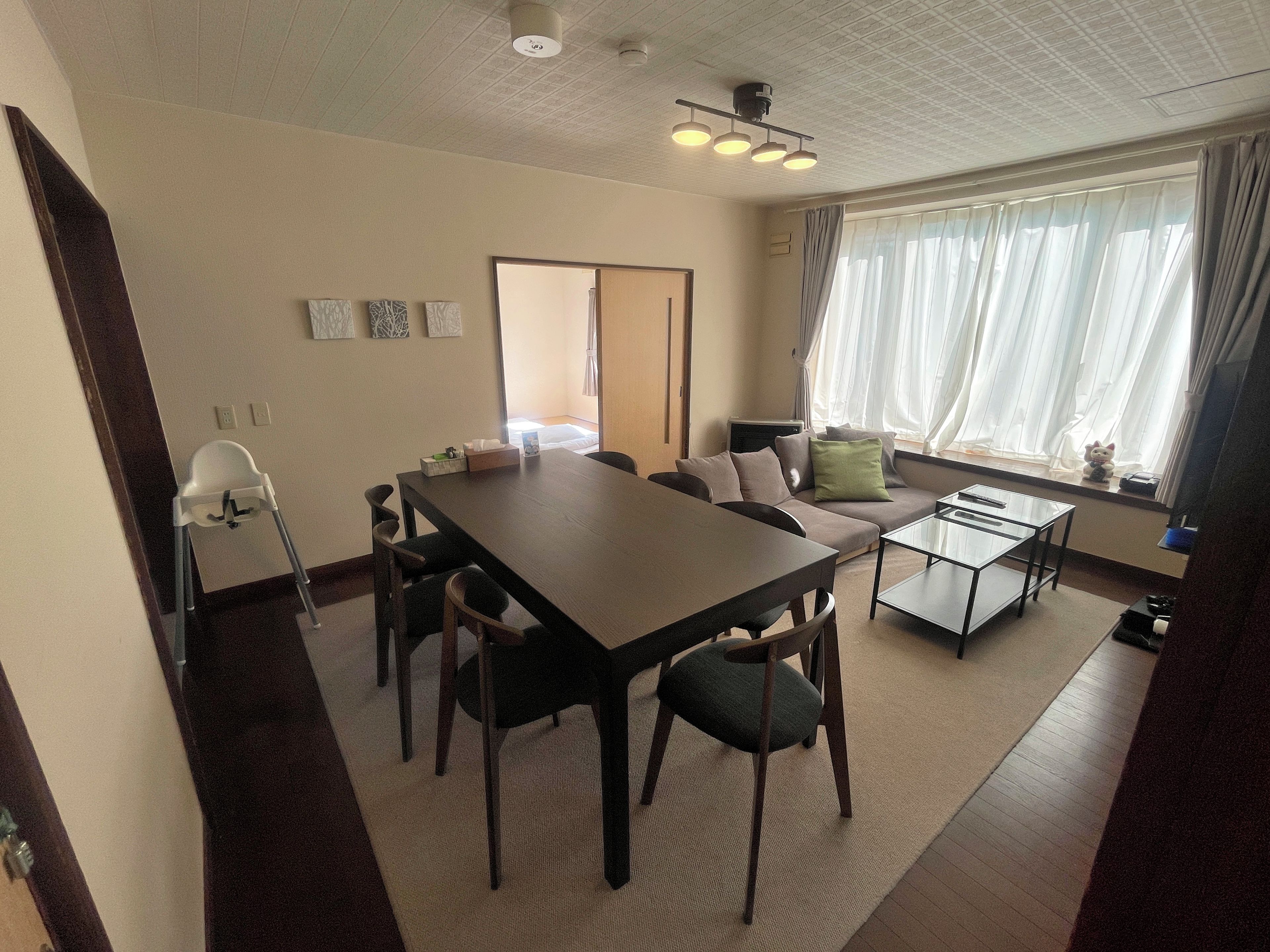 A room with a dining table, chairs, a sofa, a small coffee table, and a window with curtains.