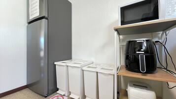 Une petite cuisine équipée d’un réfrigérateur, d’un four à micro-ondes, d’une machine à café et de poubelles.