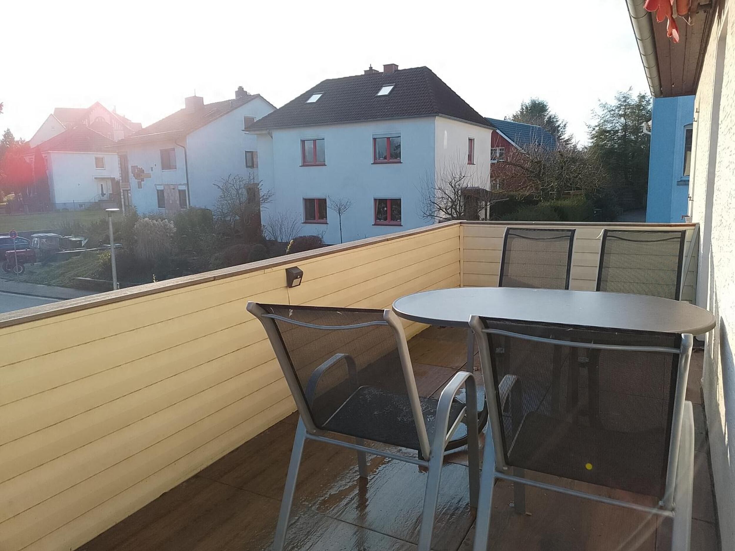 A balcony with a table and chairs, overlooking a residential area with houses and a street.