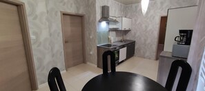 A compact kitchen with a stove, sink, and a coffee machine. There is a dining table with chairs.