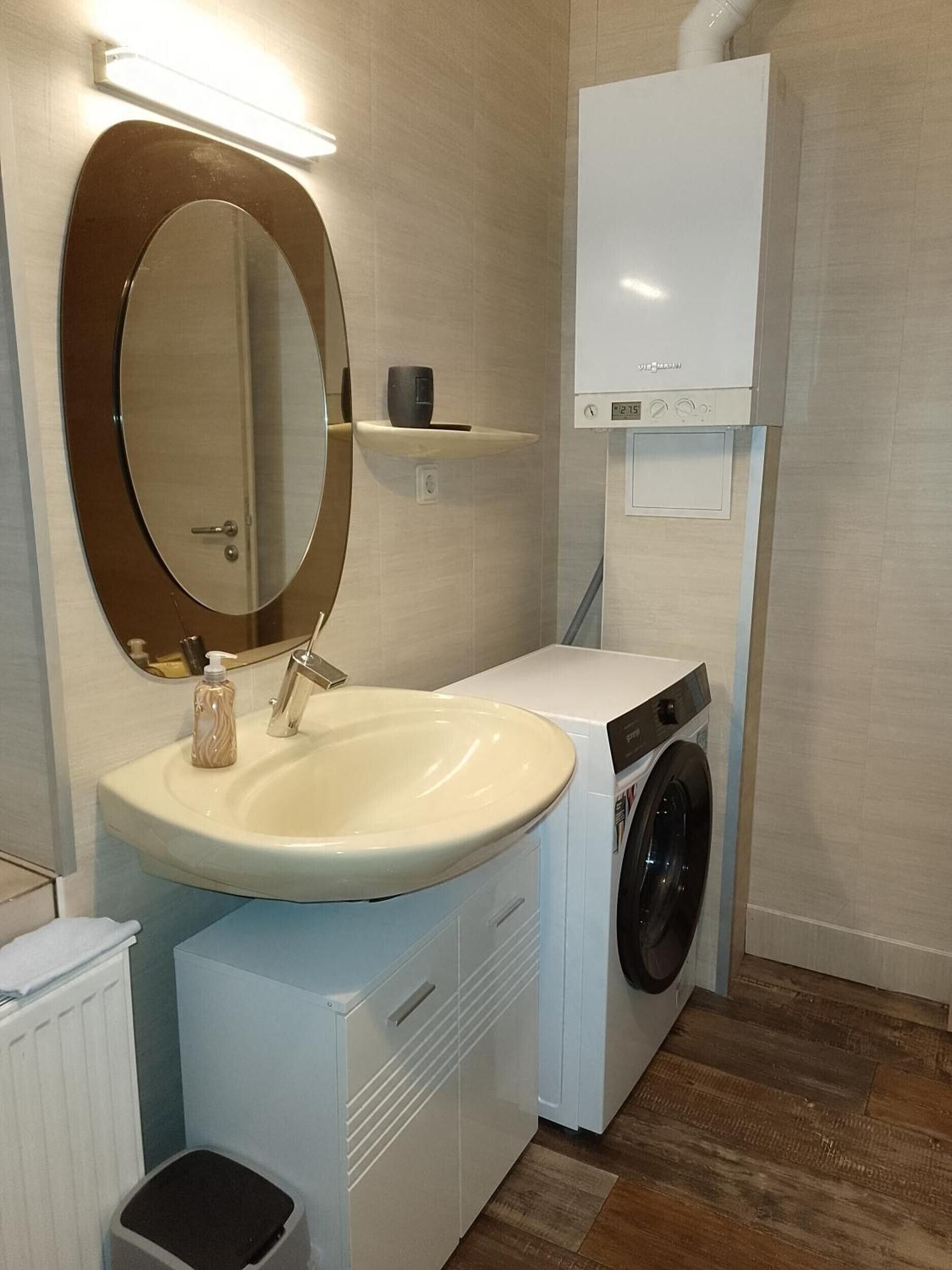 Un bagno compatto con lavandino, specchio, lavatrice e un piccolo ripiano.
