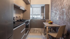 A compact kitchen with modern appliances, a dining area with a table and chairs, and a window with blinds. - MoHost - Lube (Brasov)