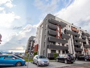 A multi-story residential building with balconies, parked cars, and a clear sky. - MoHost - Lube (Brasov)