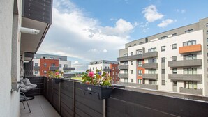 A balcony with a view of modern apartment buildings, a chair, and potted plants. - MoHost - Lube (Brasov)