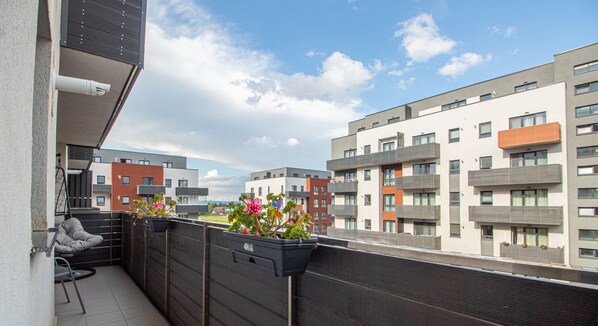 A balcony with a view of modern apartment buildings, a chair, and potted plants. - MoHost - Lube (Brasov)