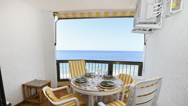 Un balcon avec une table dressée pour quatre personnes, des chaises, une petite table et une vue sur la mer.