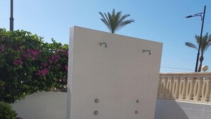 A tiled outdoor area with a white wall, a drainage grate, and a palm tree in the background. - Attractive Apartment in El Campello in Beachfront (El Campello)