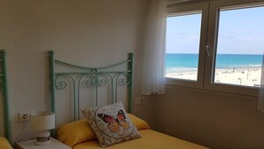A bedroom with two beds, a ceiling fan, a window with a beach view, and a bedside table with a lamp. - Attractive Apartment in El Campello in Beachfront (El Campello)