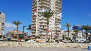 A high-rise hotel with multiple balconies, a sandy beach in the foreground, and palm trees. - Attractive Apartment in El Campello in Beachfront (El Campello)