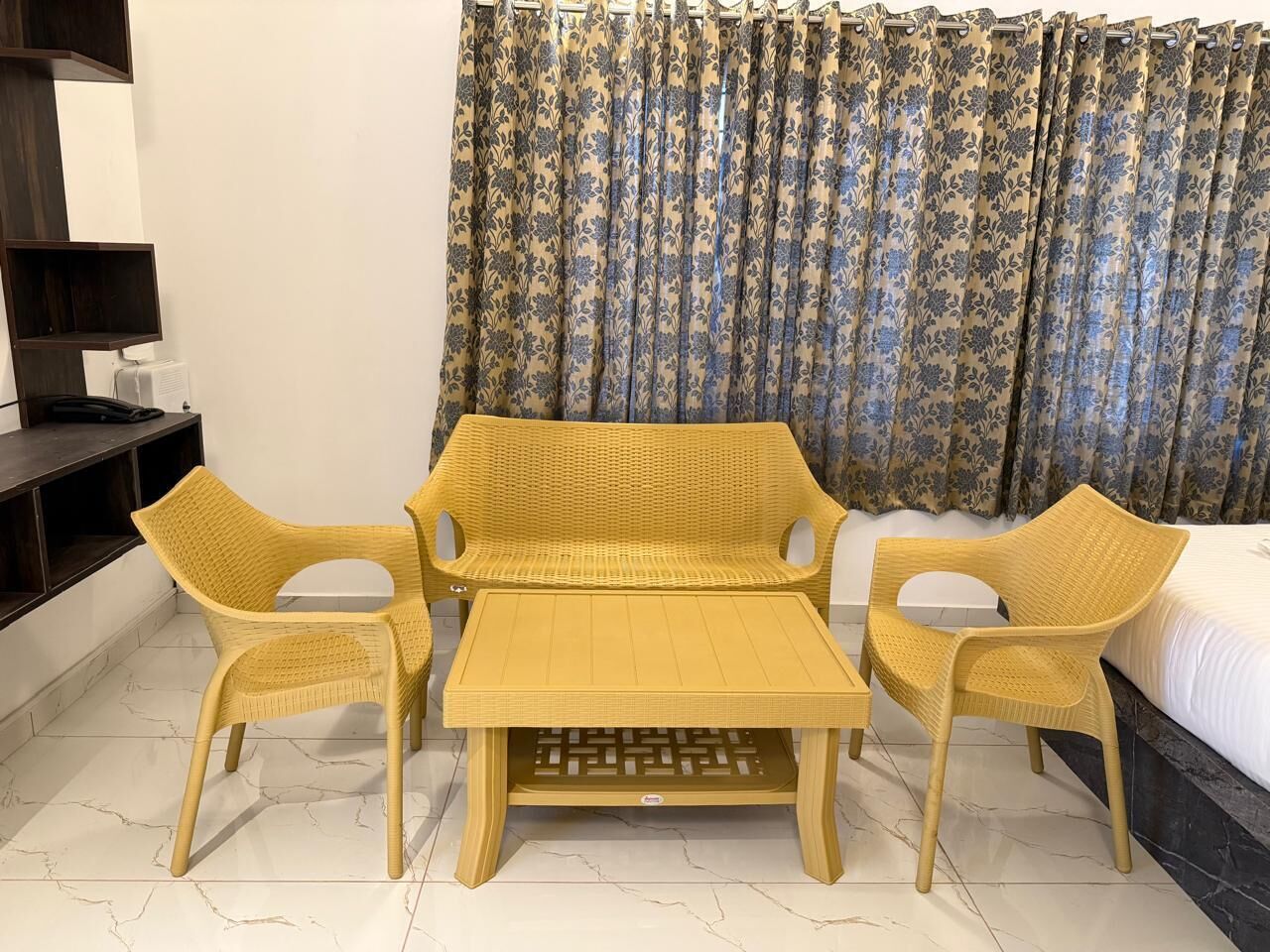 A hotel room with a bed, a small table, two chairs, a TV, and a shelf.