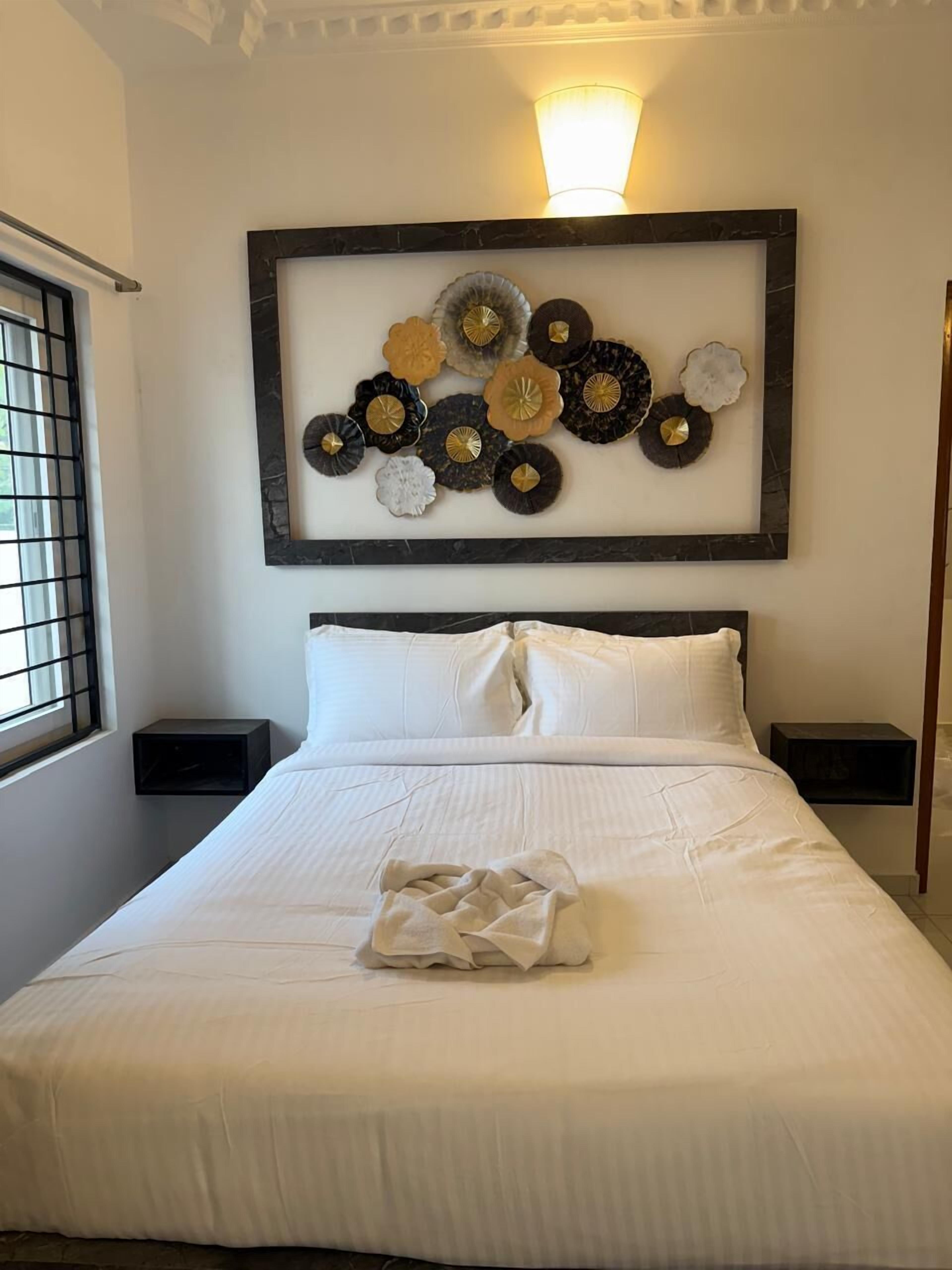 A neatly made bed with white linens, a decorative wall art piece above it, and two bedside tables with black surfaces.