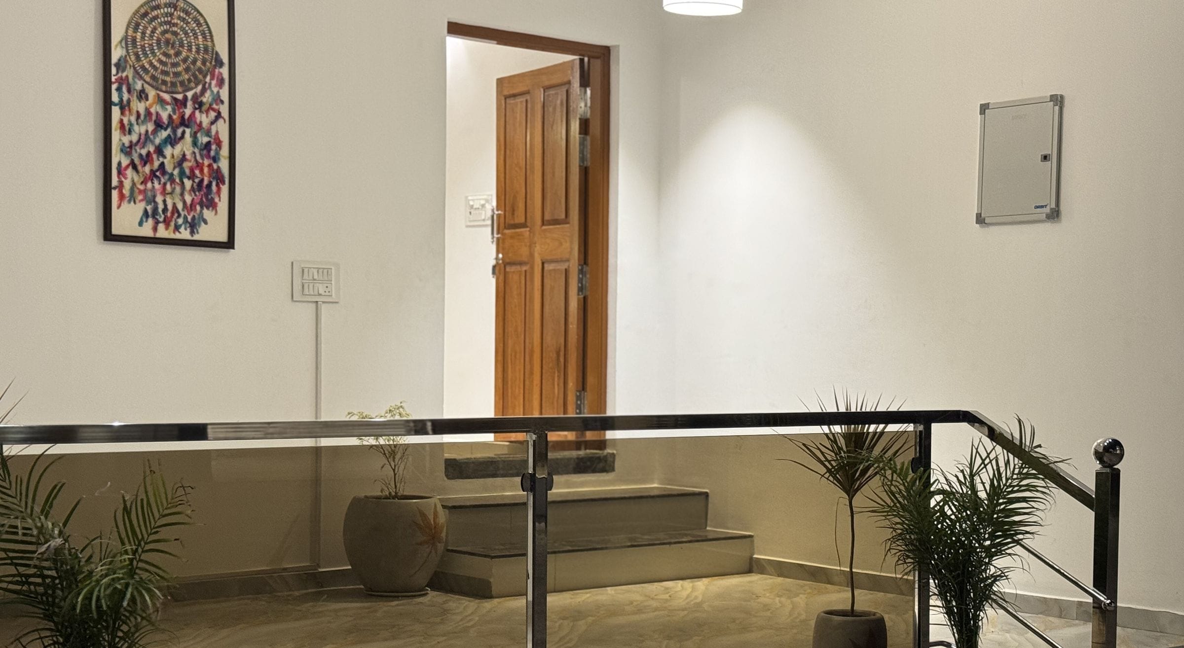 Un hall d’hôtel avec une rambarde en verre, une porte en bois et des plantes en pot.