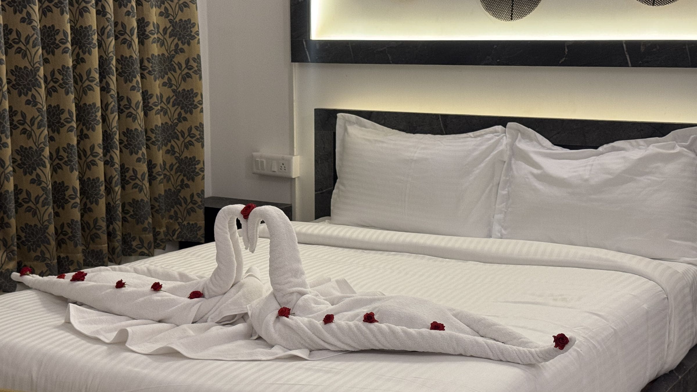 A hotel room with a neatly made bed, a headboard, and a floral curtain.
