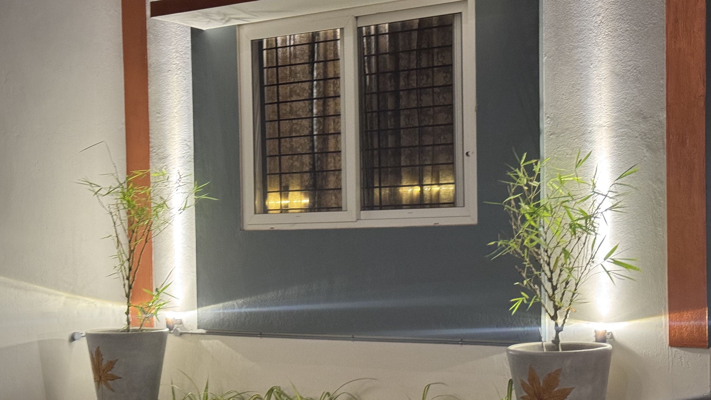 A building exterior with a window, two potted plants, and a grassy area.