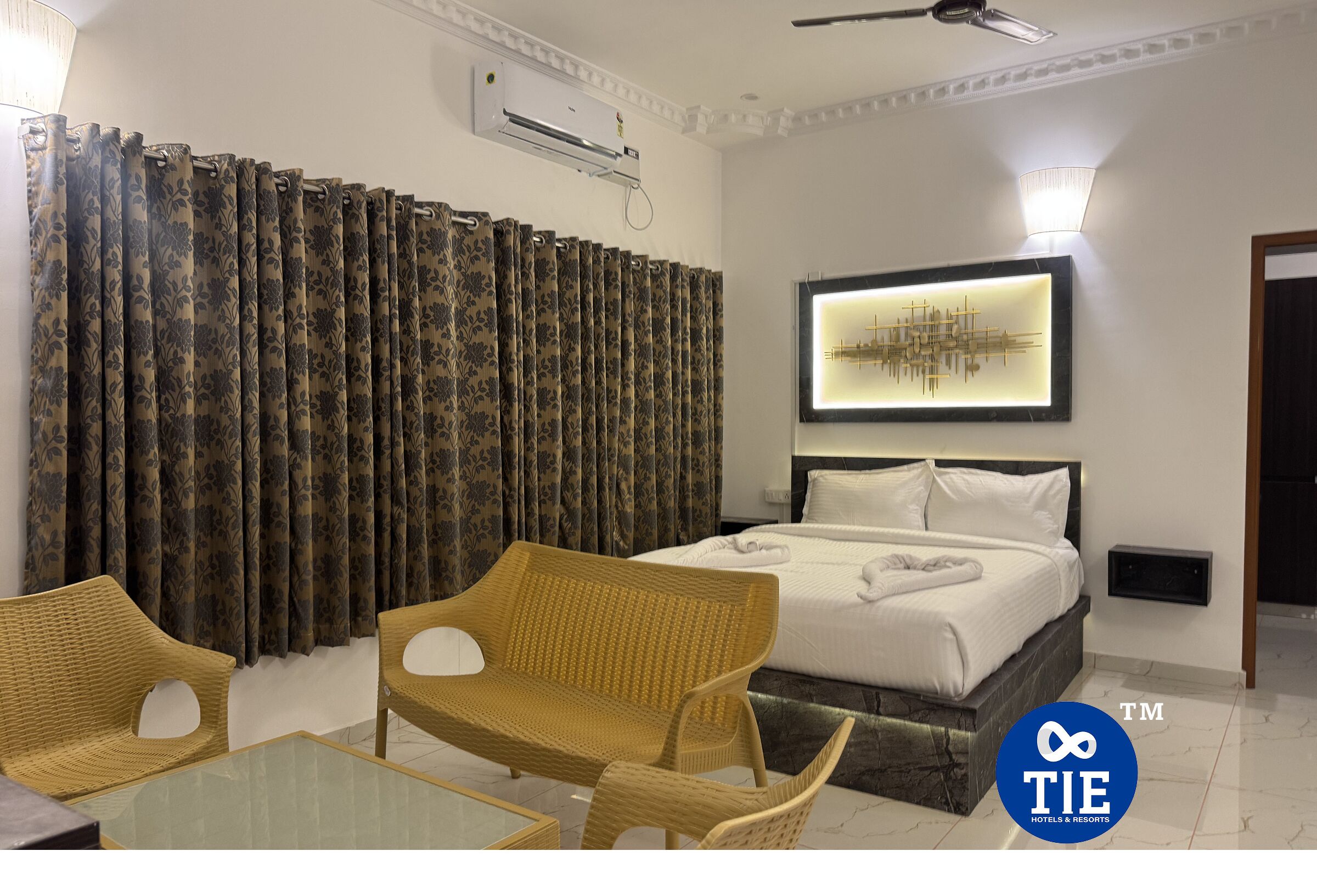 A hotel room with a bed, a sofa, a glass table, and curtains.