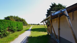 A pathway leading to a building with a sloped roof supported by bamboo poles. - Safari Tent in Netherlands near Dunes & Sea (Hollum)