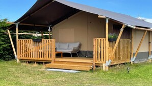 A tented accommodation with a wooden deck, a sofa, and a window. - Safari Tent in Netherlands near Dunes & Sea (Hollum)