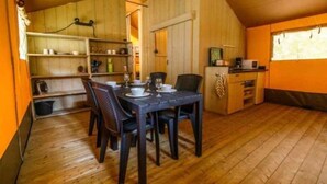 A compact kitchen with wooden cabinets, a dining table with chairs, and a small refrigerator. - Safari Tent in Netherlands near Dunes & Sea (Hollum)