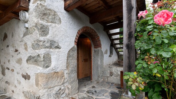 Un bâtiment en pierre doté d’une porte en bois, d’un escalier en pierre et d’une structure en poutres de bois.