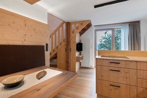 Een moderne keuken met houten kasten, een eettafel met een kom en een blad, en een trap die naar een andere kamer leidt.