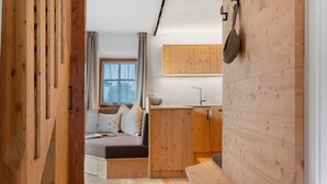 A compact room with a bed, a small kitchenette, and a wooden wall.