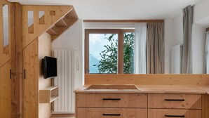 A modern kitchen with wooden cabinetry, a built-in TV, and a large window with a view of trees and mountains.