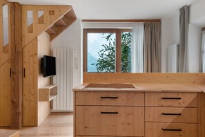 Una cucina moderna con mobili in legno, TV integrata e un'ampia finestra vista alberi e montagne.