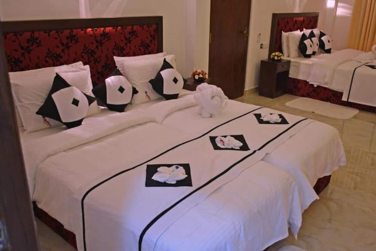 Ein Hotelzimmer mit zwei Betten, jeweils mit rotem Kopfteil und weißer Bettwäsche. Auf den Betten liegen dekorative Kissen und ein Plüschtier.