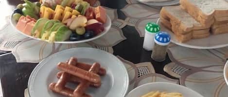 A dining table with various food items including sausages, fries, and a plate of fruit.