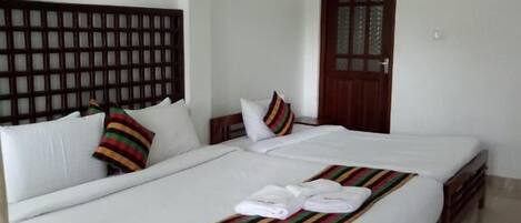 Habitación de hotel con una cama grande, cabecera de madera, ventilador de techo y puerta con un panel de vidrio.