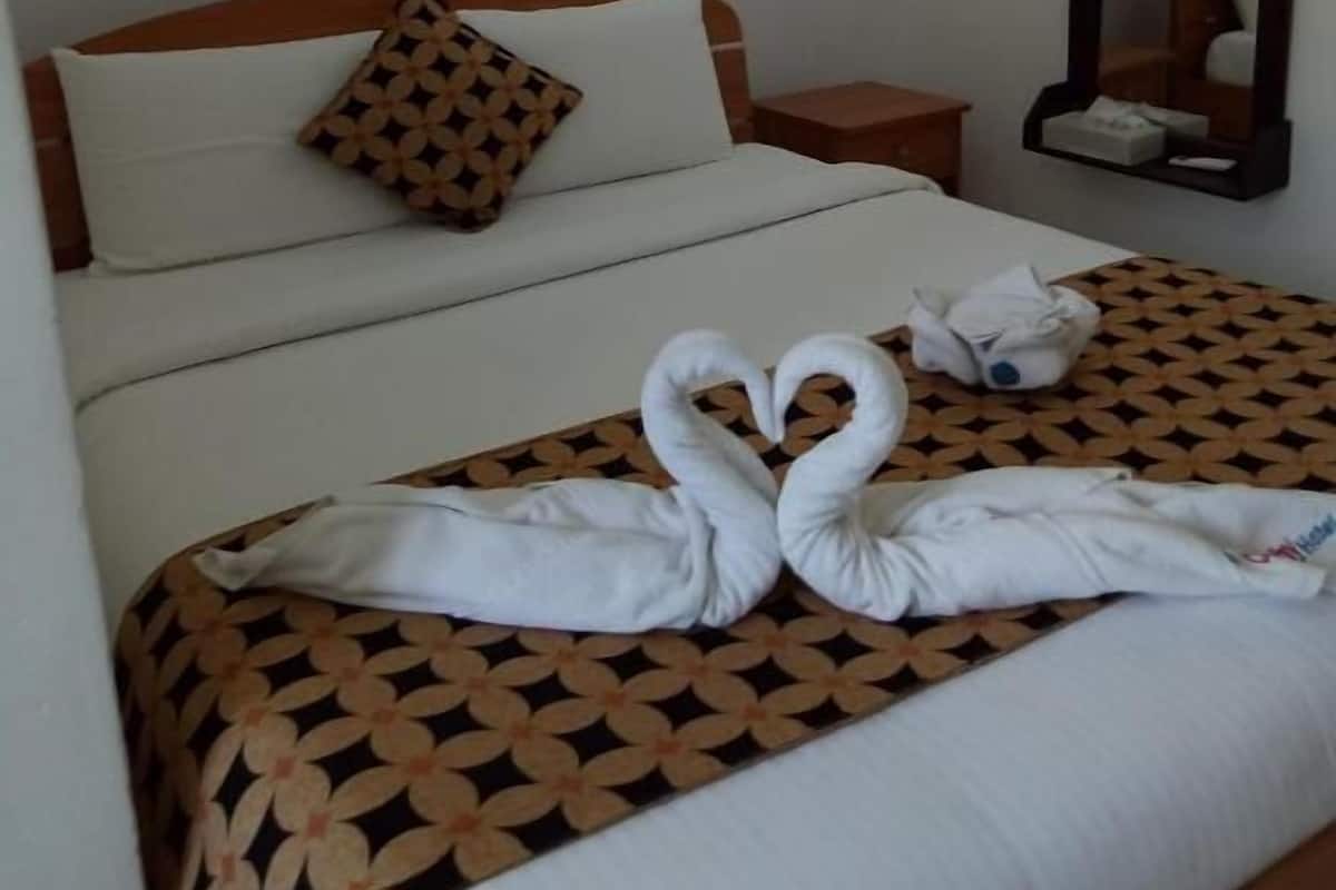Ein Hotelzimmer mit einem ordentlich bezogenen Bett, einer gemusterten Tagesdecke, einem Kissen, einem Nachttisch, einem Spiegel und einer Wandleuchte.