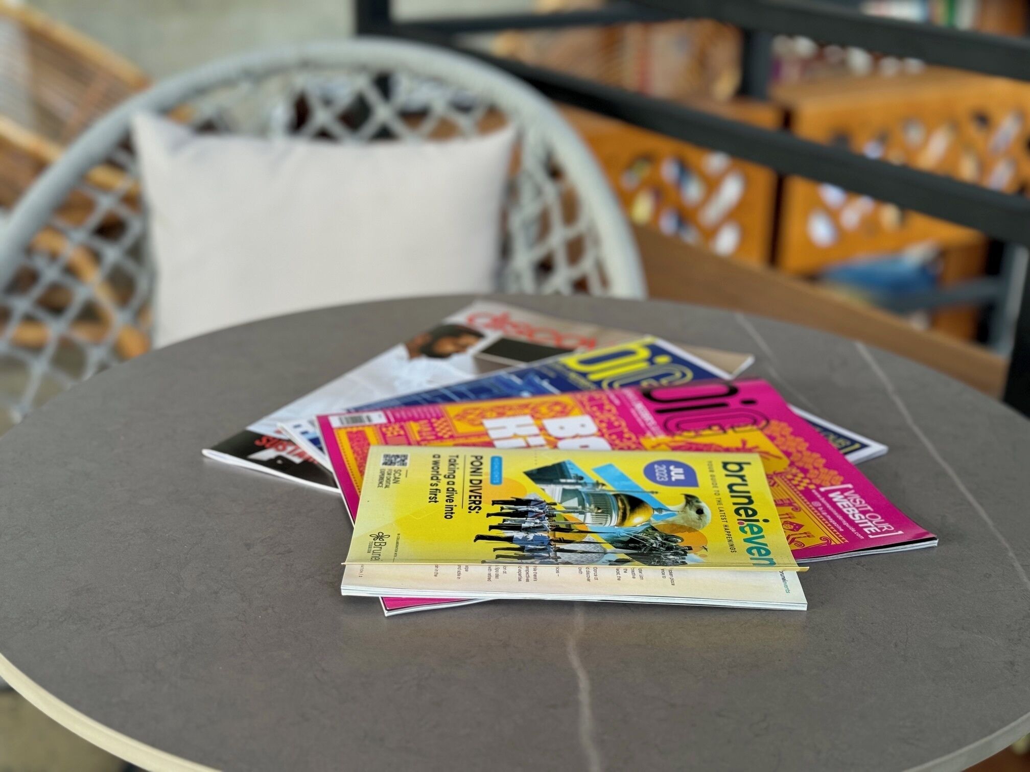 Una mesa redonda con revistas y un almohadón.