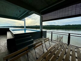 Terraza exterior con piscina, bancos de madera y vistas a un lago y colinas boscosas.