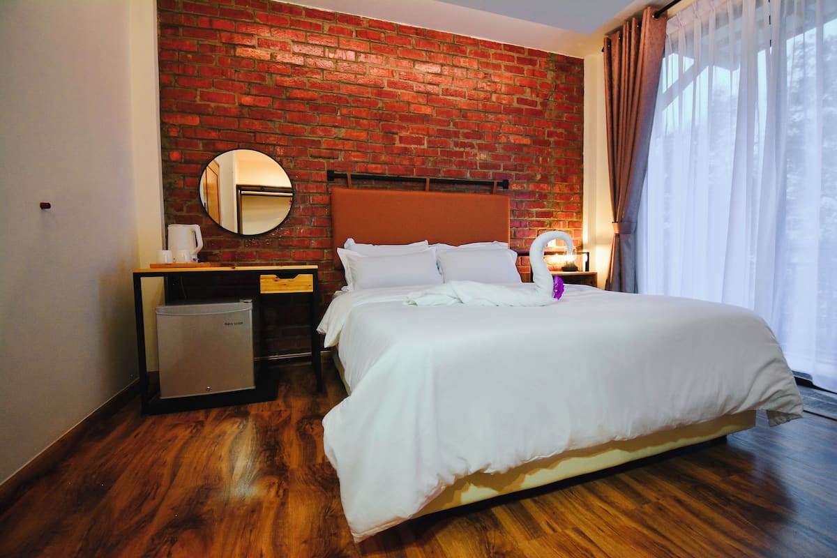 Une chambre d’hôtel avec un mur en briques, un lit avec une literie blanche, un miroir rond, une petite table avec une machine à café et une table de chevet avec une lampe.