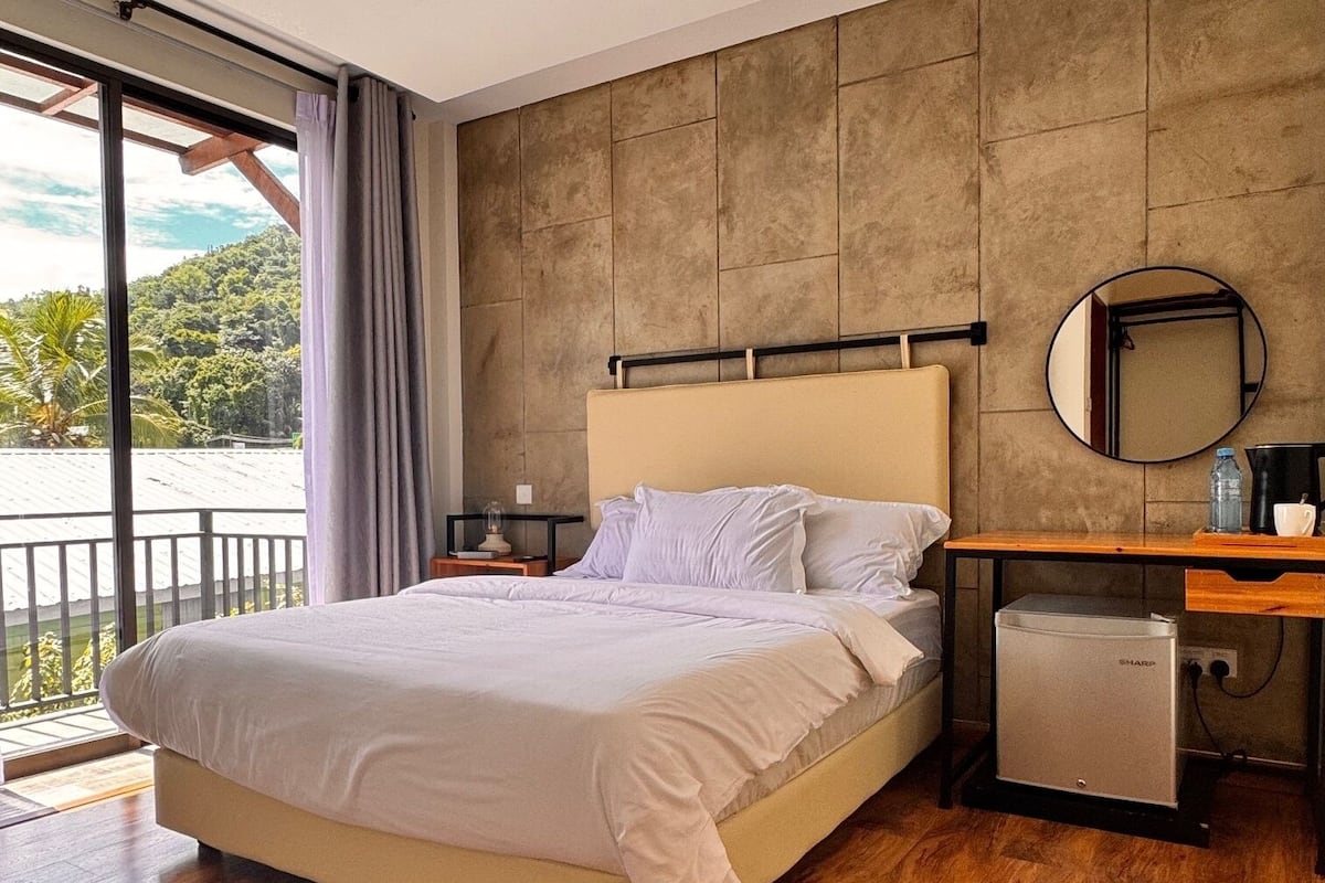 Une chambre moderne dotée d’un grand lit, d’un parquet en bois, d’un bureau intégré et offrant une vue sur un paysage luxuriant.
