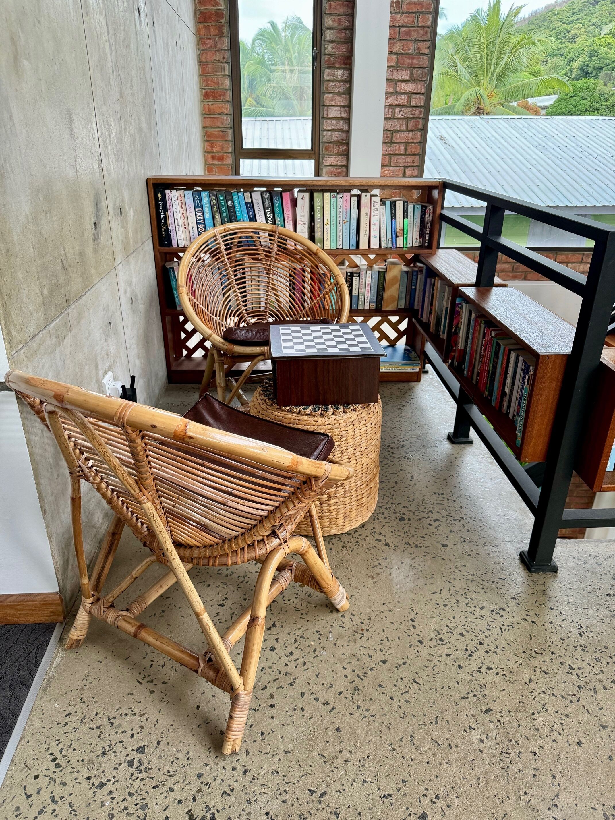 Eine gemütliche Leseecke mit einem Korbstuhl, einem kleinen Holztisch und einem Bücherregal voller Bücher.