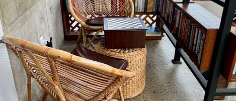Un rincón acogedor para leer, con un sillón de mimbre, una mesita de madera y una estantería llena de libros.