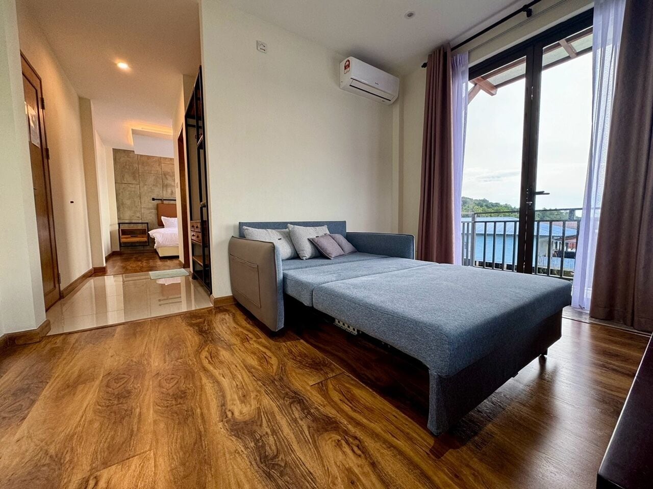 A modern hotel room with a bed, a sofa, a small table, and a balcony with a view.