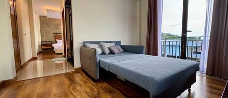 A modern hotel room with a bed, a sofa, a small table, and a balcony with a view.