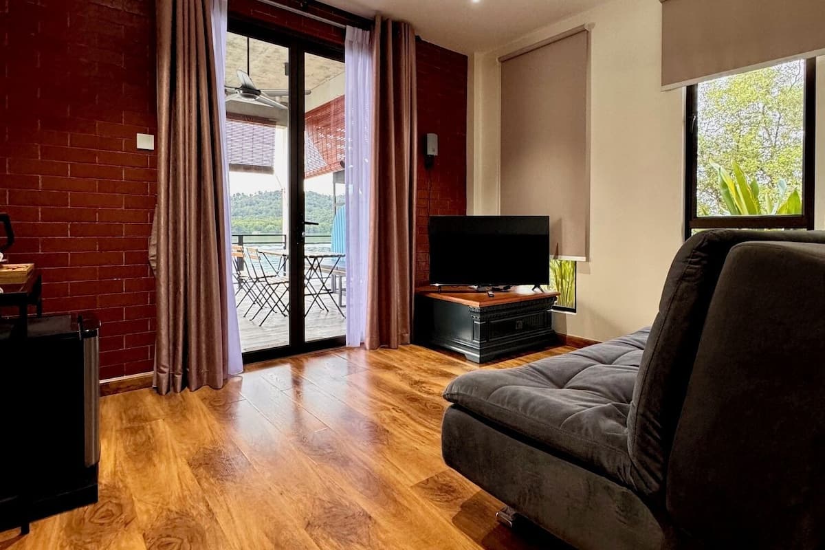 Un salon avec un canapé, un téléviseur et un ventilateur de plafond. Une porte-fenêtre coulissante donne accès à un espace extérieur.