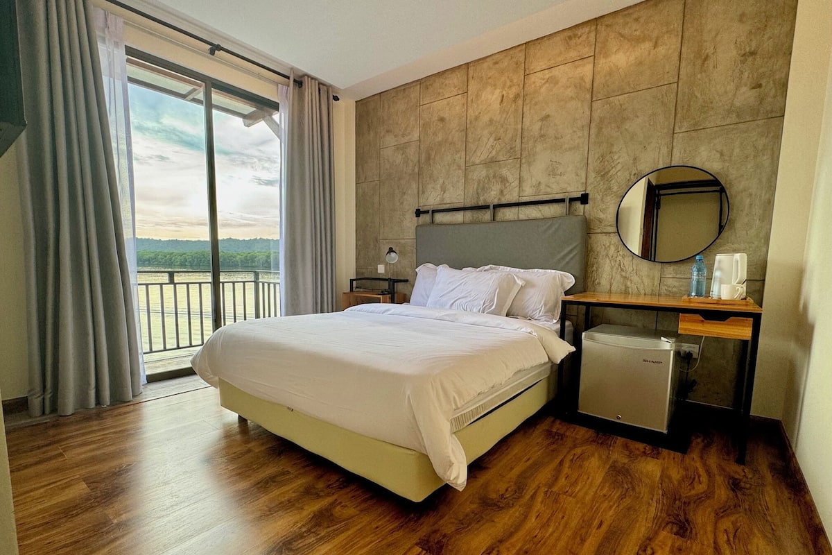 Une chambre d’hôtel comprenant un lit, une table de chevet, un petit réfrigérateur, un miroir et une vue sur l’extérieur.