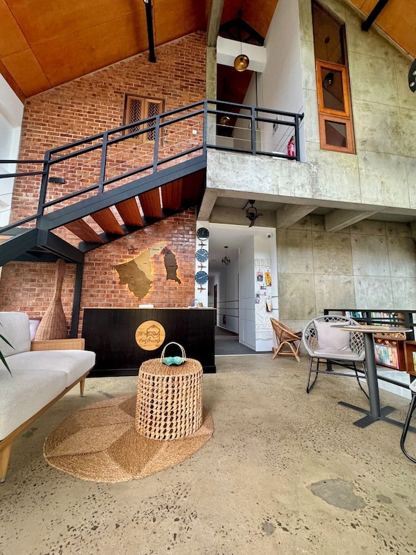 A spacious loft with exposed brick walls, a mezzanine level, a staircase, and a cozy seating area with a round woven ottoman. - Embun (Bandar Seri Begawan)