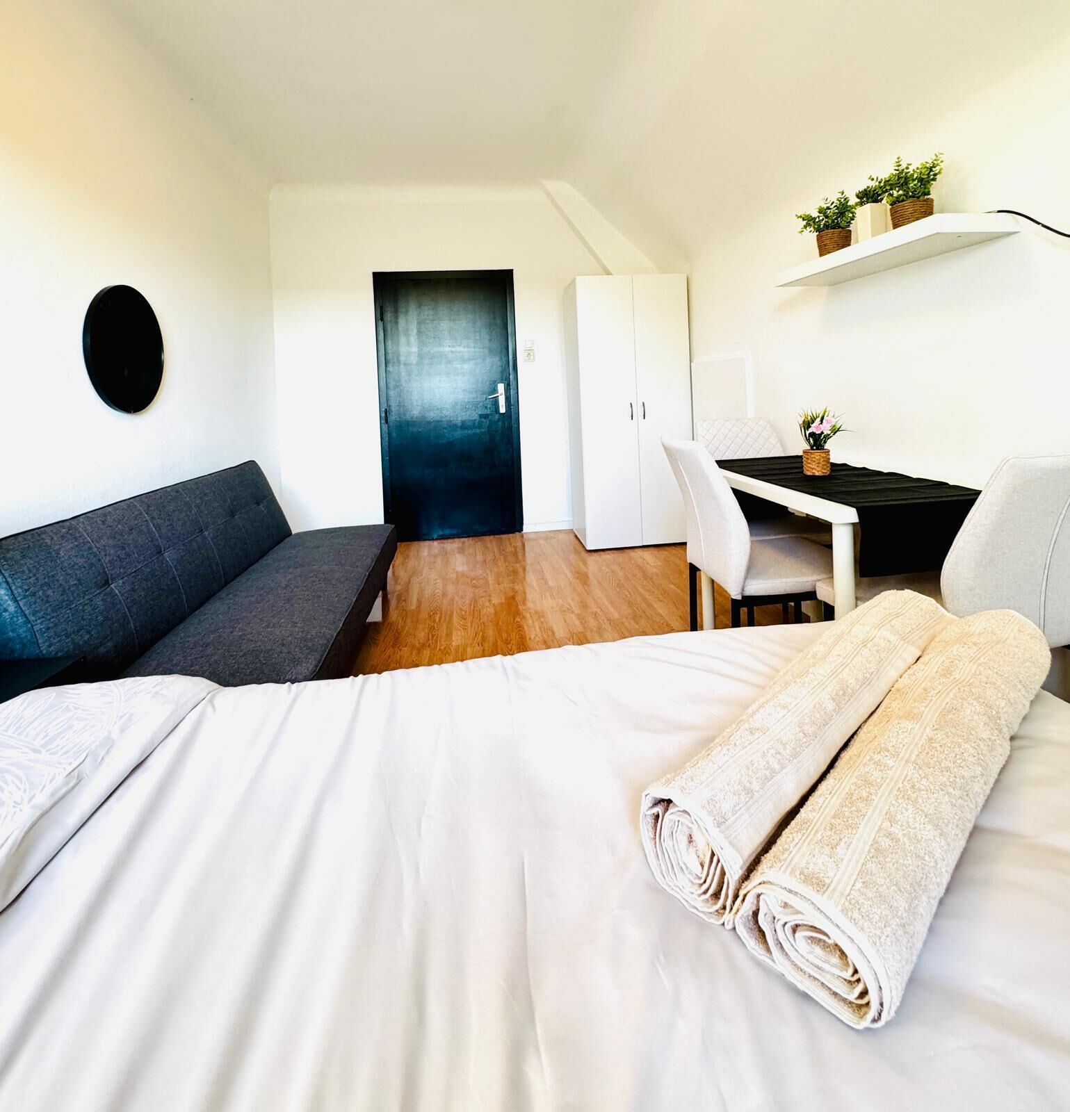 A modern hotel room with a bed, a desk, a sofa, and a door.