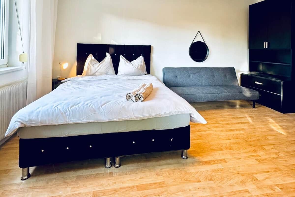 Un dormitorio moderno con una cama grande, un sofá gris, un televisor y una lámpara circular.