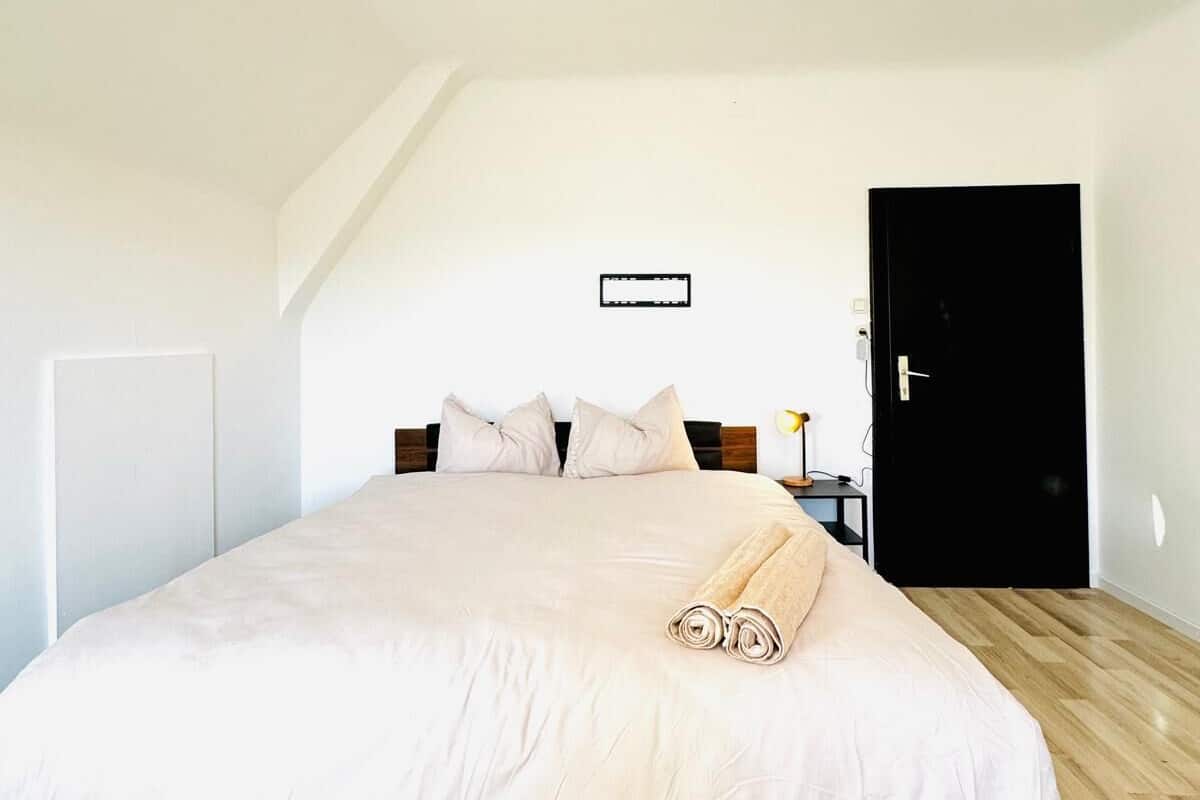 Un dormitorio con una cama grande, una mesita de noche, una lámpara y una puerta.